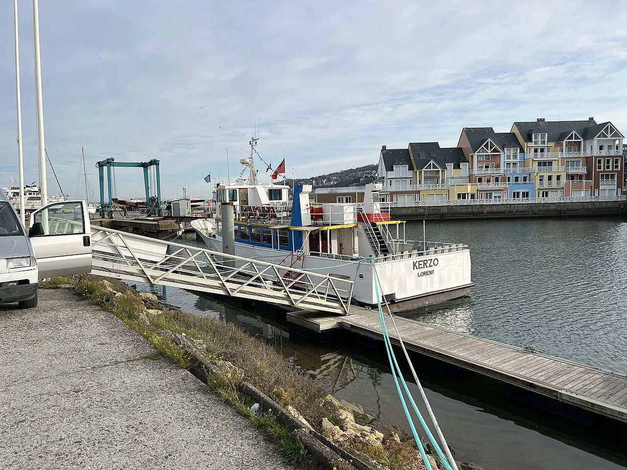 Pontoon and moored passenger boat in the Deauville marina with colourful waterside houses behind