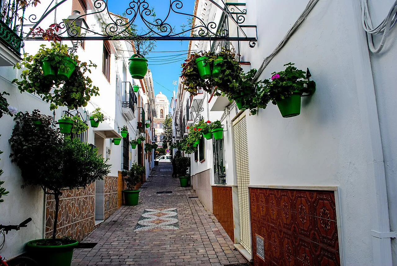 Narrow whitewashed lane hung with green flowerpots in Estepona old town, a church tower at the end