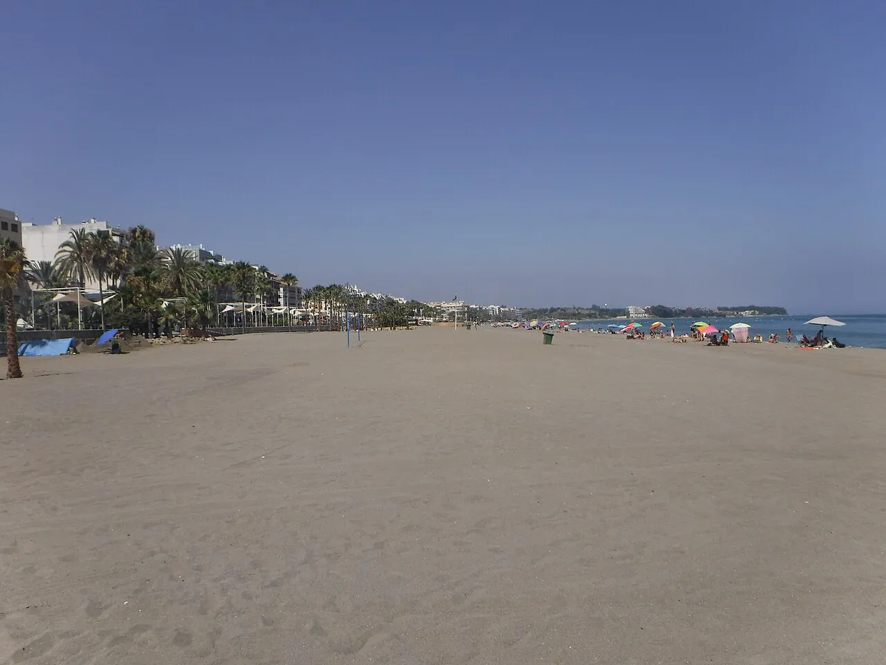Wide sandy Playa de la Rada in Estepona with palms and the seafront promenade in the distance