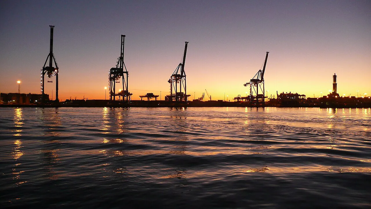 Harbour cranes and the Lanterna lighthouse silhouetted at sunset in Genoa