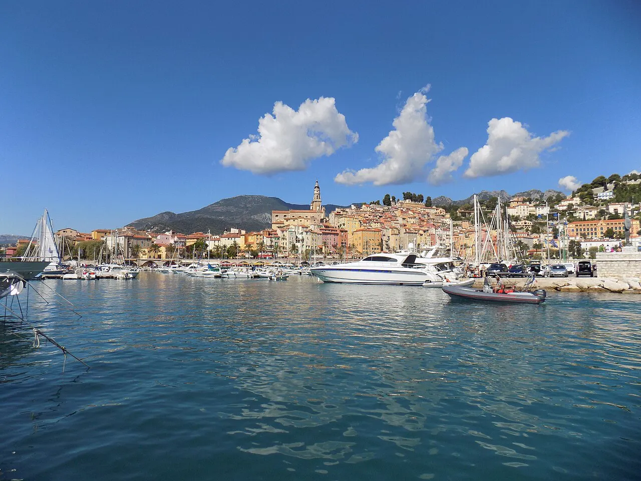 Boats in Menton’s old port with the pastel old town and basilica bell tower across the water