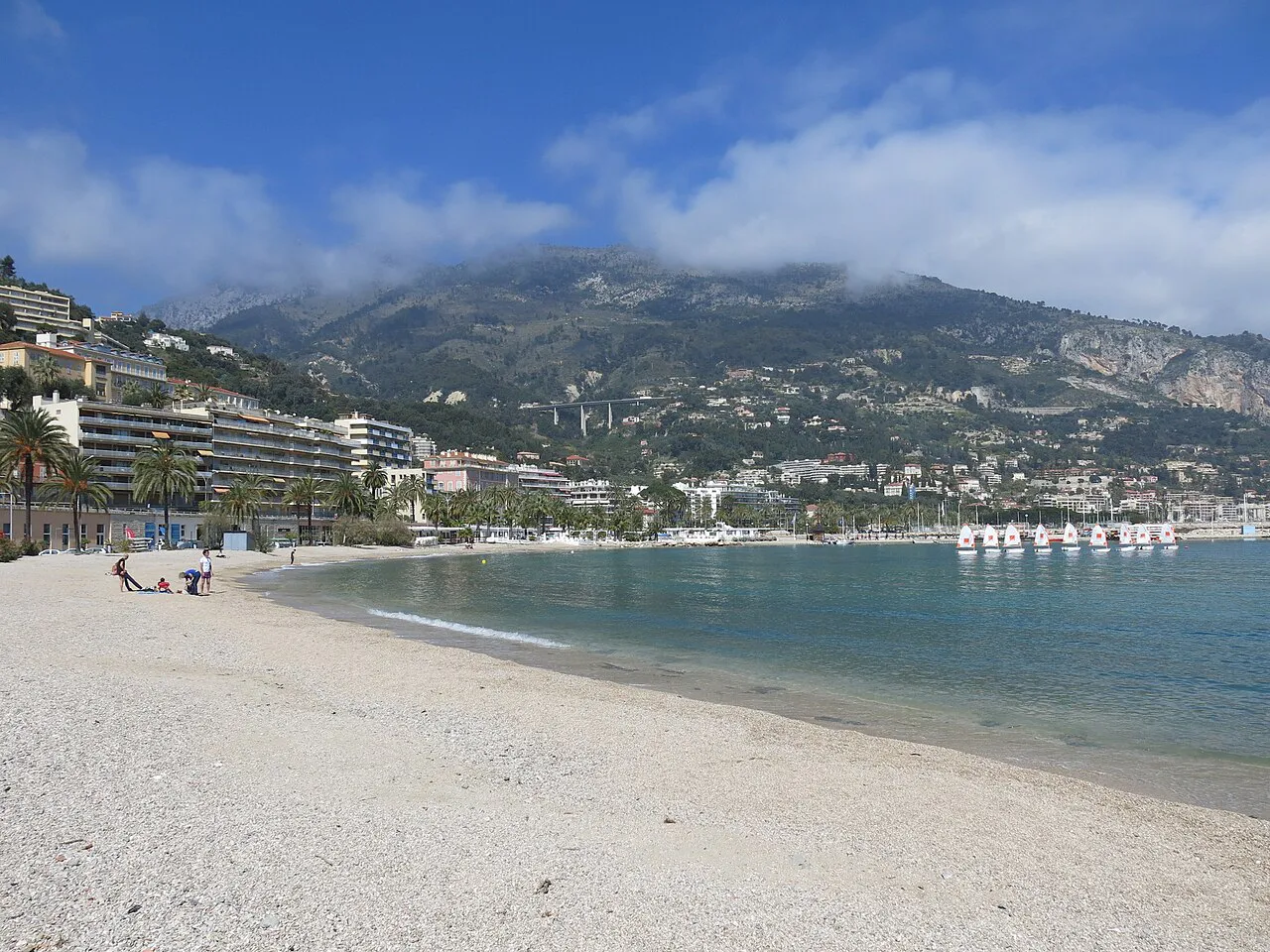 Pale sandy Plage des Sablettes curving along the bay below the mountains, Menton