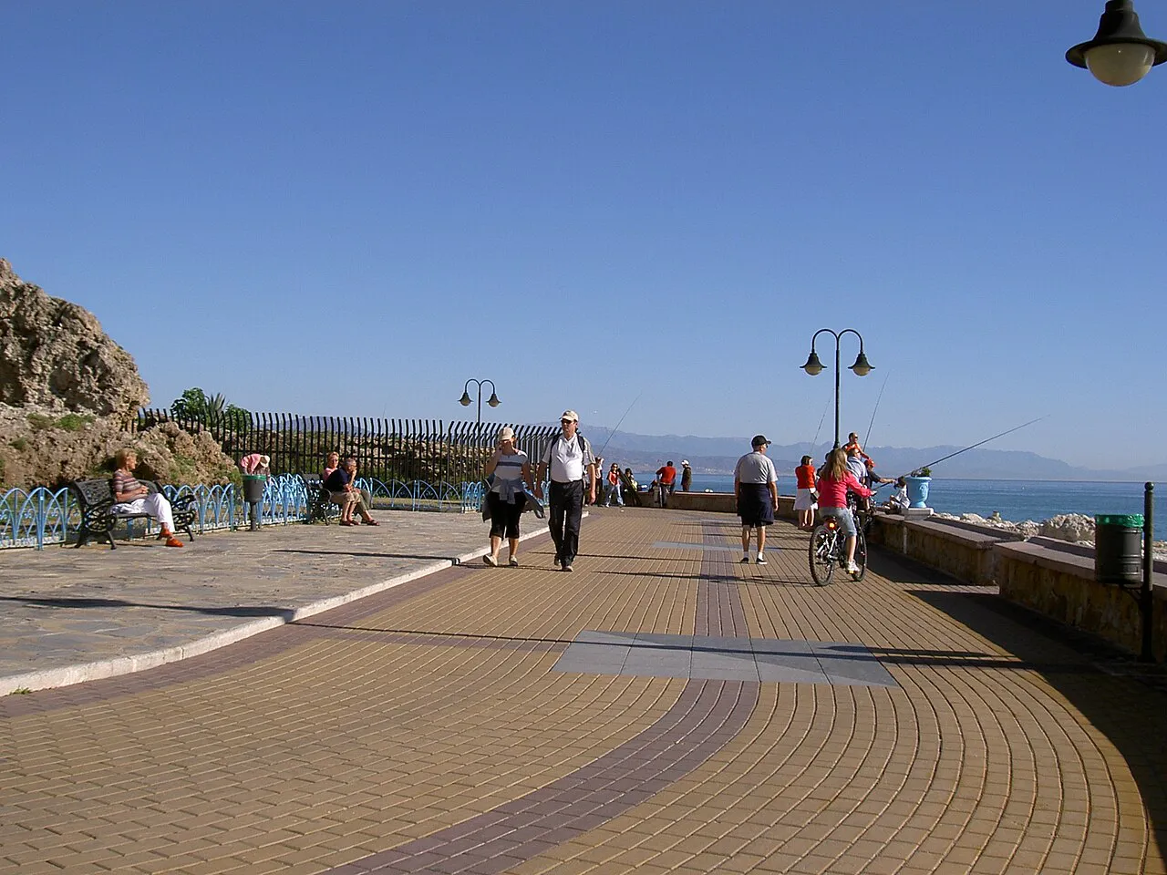 A wide paved seafront promenade beside a rocky outcrop on a sunny day in Torremolinos