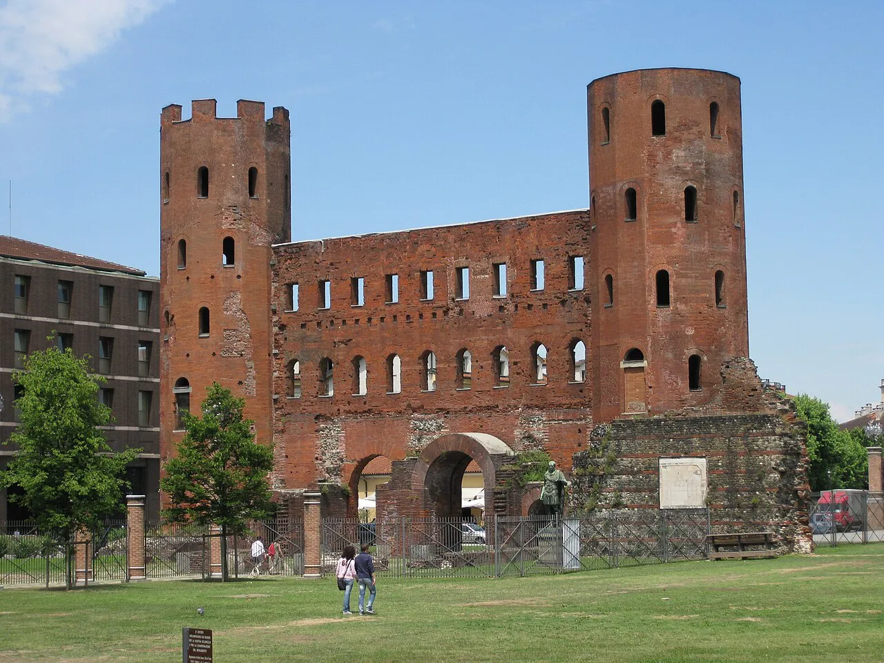 Red-brick Porta Palatina, Turin's Roman gate with twin towers, beside a green lawn