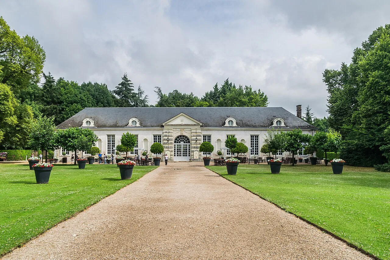 The orangery of the Château de Cheverny at the end of a gravel path between lawns and potted trees