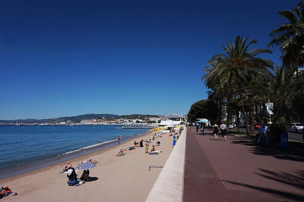 Sandy beach beside a palm-lined promenade at the eastern end of the Croisette, Cannes, under a blue sky