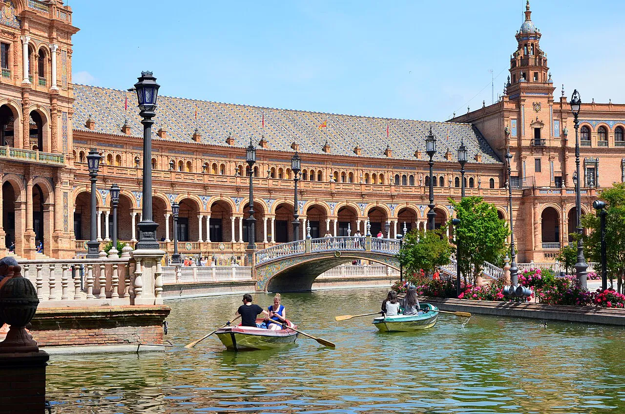 Rowing boats on the canal in front of the brick arcades and towers of Plaza de España, Seville