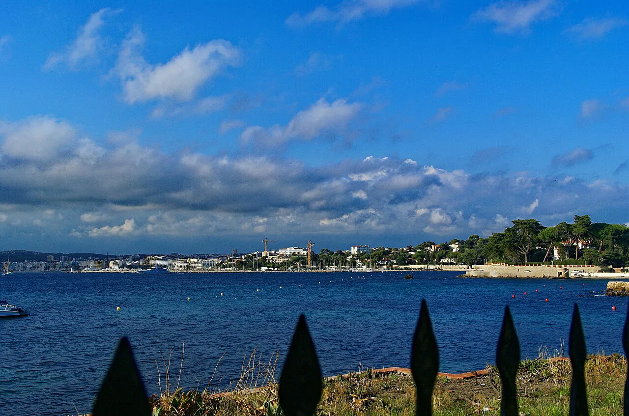 Blue bay of Juan-les-Pins under scattered clouds, looking across to the wooded Cap d'Antibes