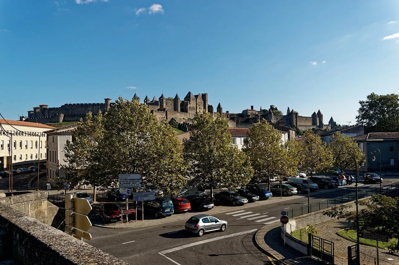 Parked cars on a lower-town street in Carcassonne with the walled Cité on the hill behind trees