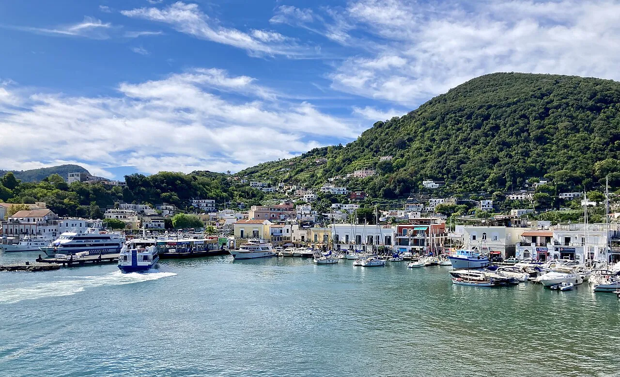 Ischia Porto harbour with ferries and boats below a green wooded hill