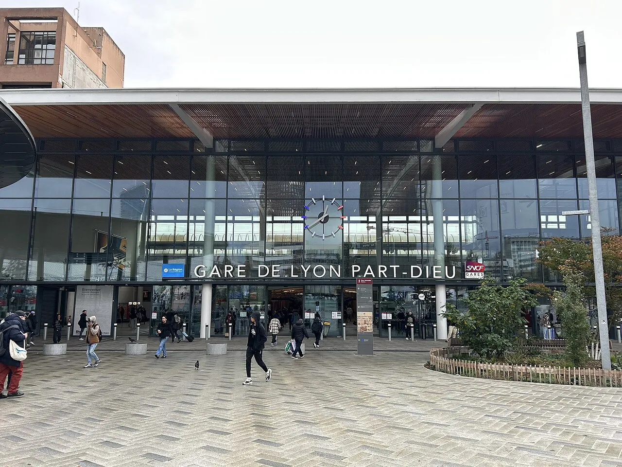 Glass main entrance of Lyon Part-Dieu railway station under a wide timber canopy, with a paved forecourt