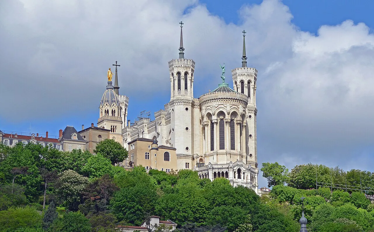White towers of the Basilica of Notre-Dame de Fourvière above green trees on Fourvière hill, Lyon