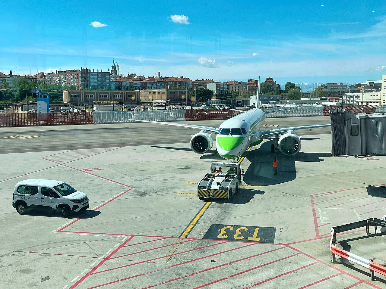 Aircraft parked at a gate on the Madrid-Barajas apron with the rooftops of Barajas district behind