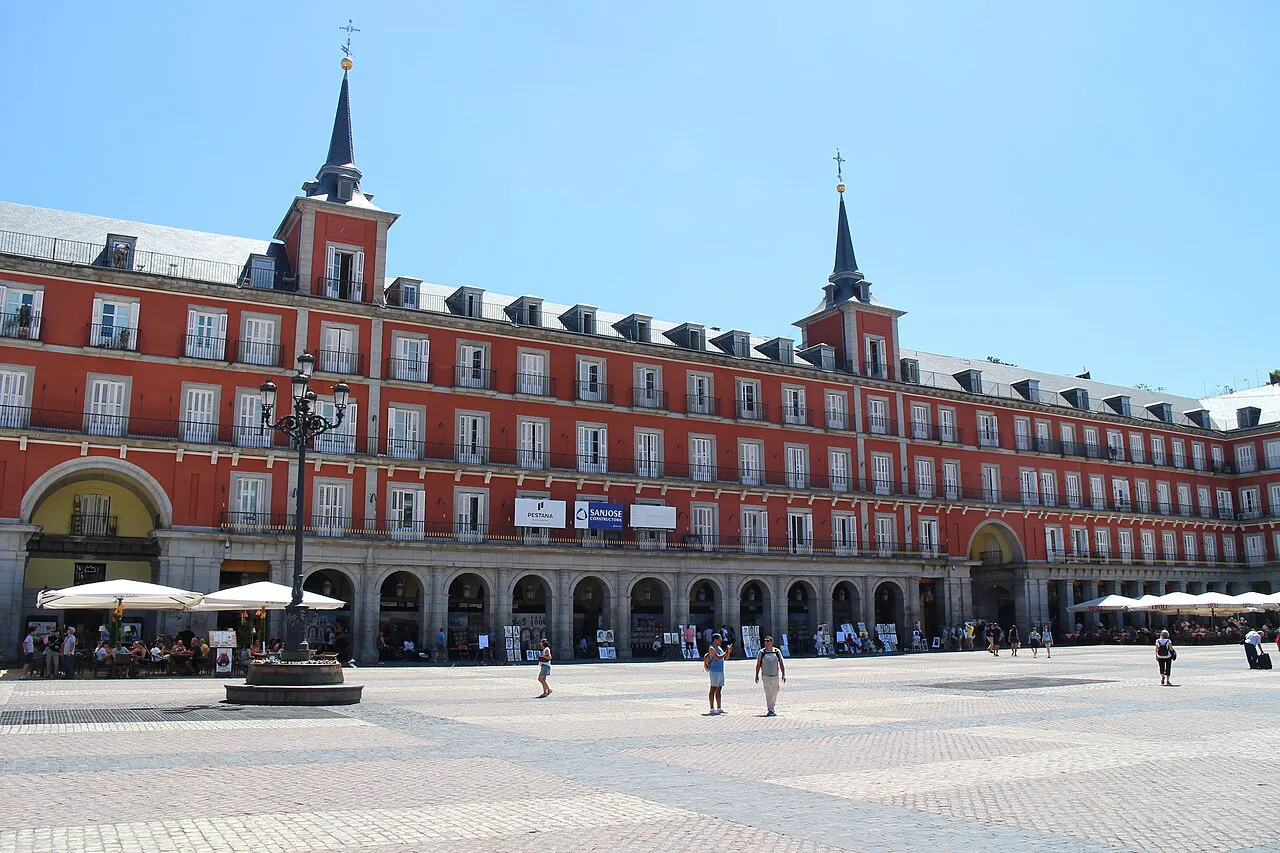 Red-fronted arcaded buildings and twin spires around the wide open Plaza Mayor in Madrid on a sunny day