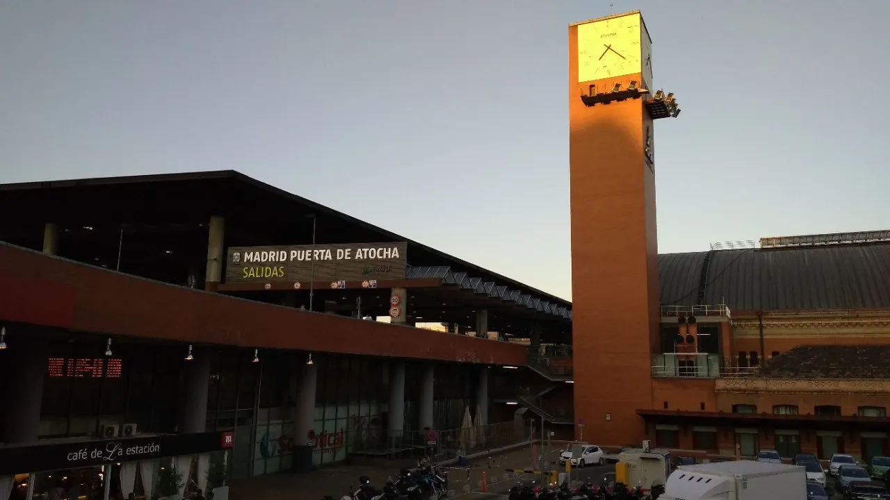 Brick clock tower and modern entrance of Madrid Puerta de Atocha station at dusk