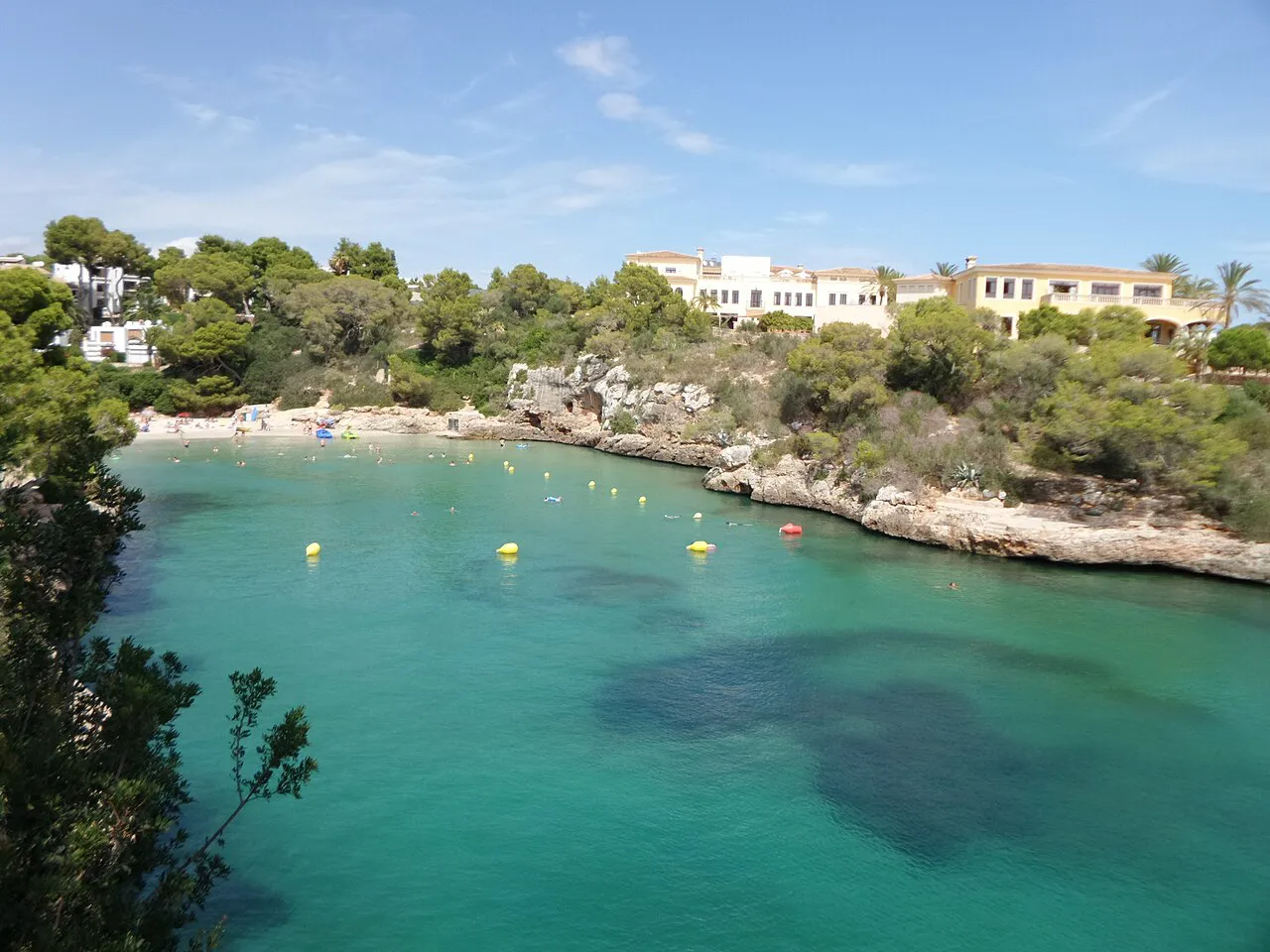 Turquoise water in the rocky bay of Cala Ferrera, edged by pines and low villas