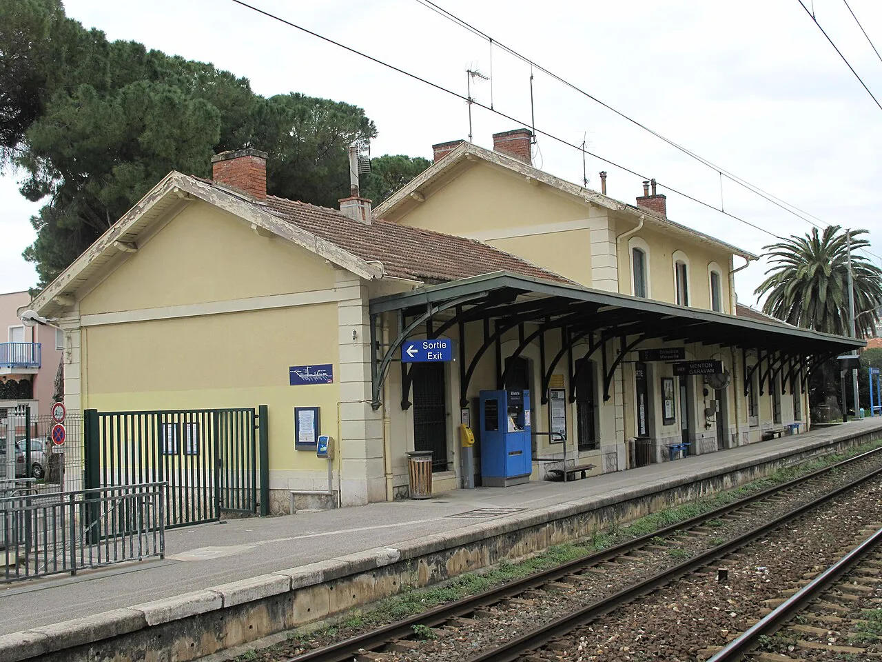 Platform and yellow station building of Menton-Garavan railway station beside the tracks
