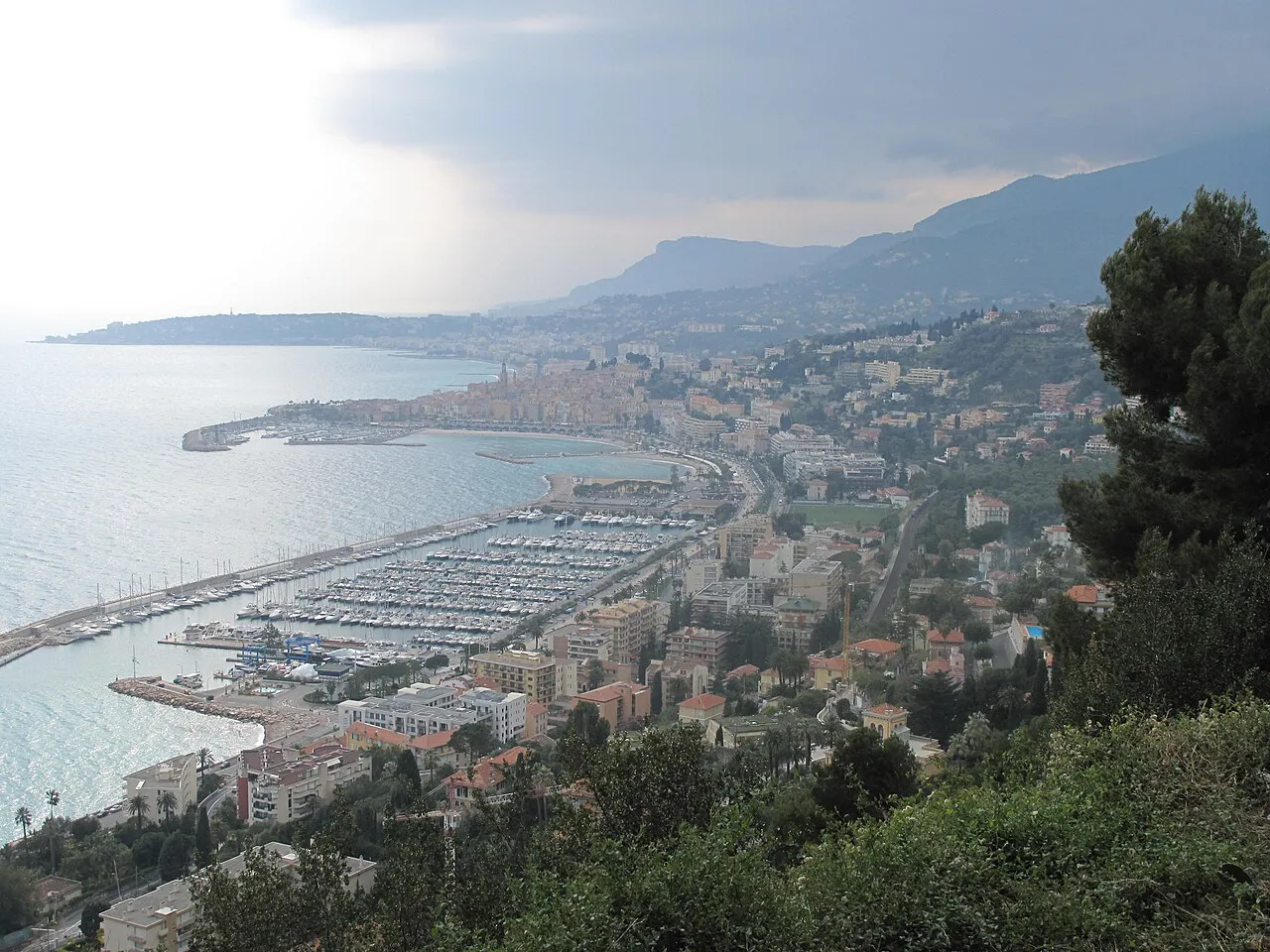Wide hillside view over Menton's marina, seafront and old town curving along the coast towards the mountains