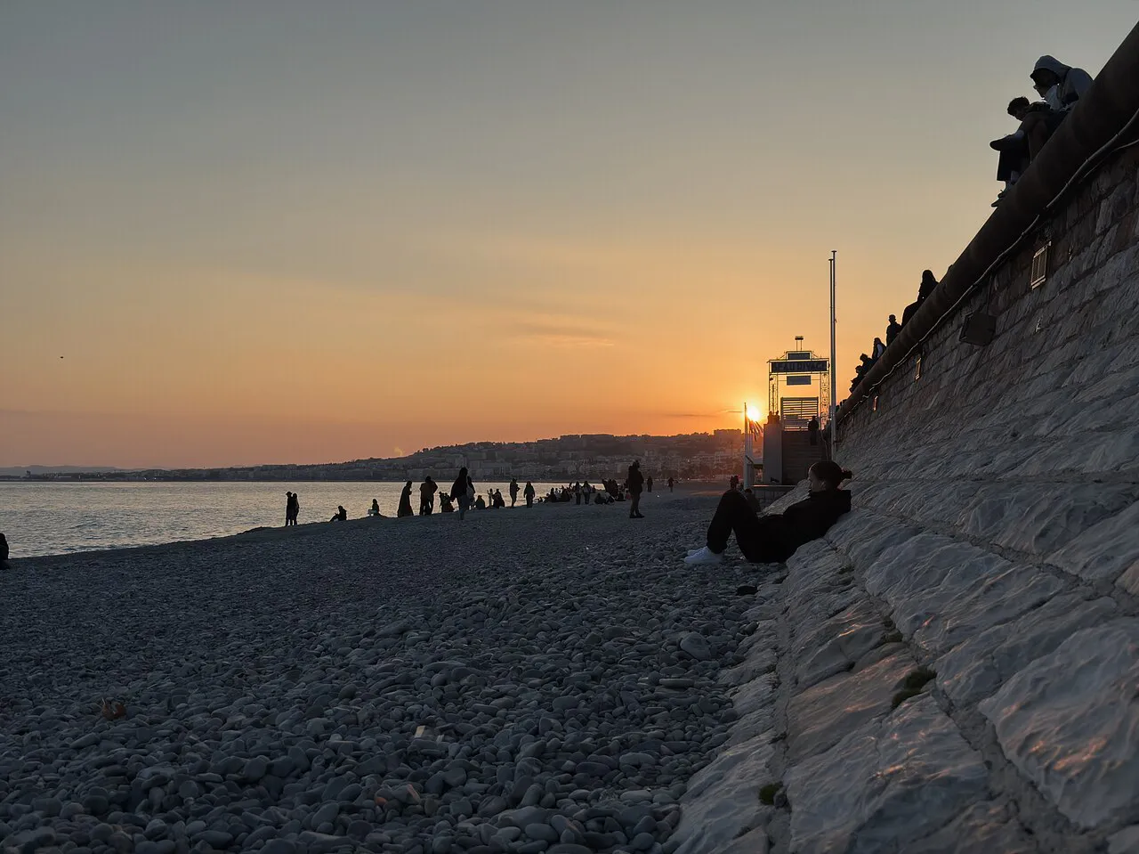 Sunset over the pebble beach of Nice with a lifeguard tower below the Promenade des Anglais wall