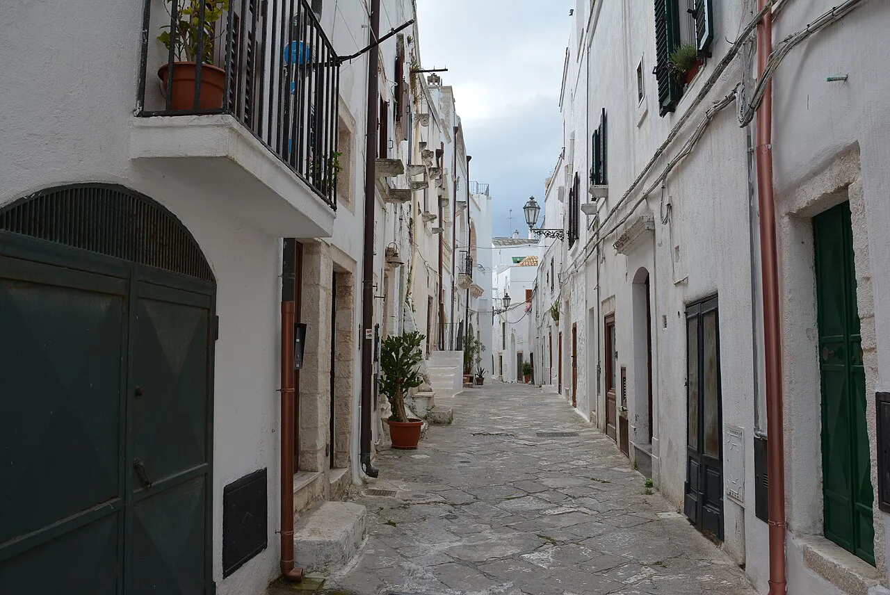Whitewashed lane in Ostuni's old town with stone paving, green doors and balconies