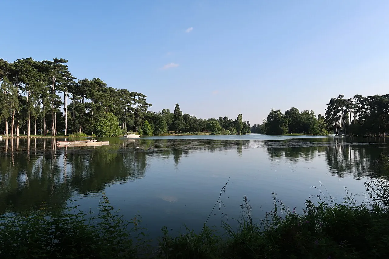Calm water of the Lac Inférieur ringed by trees in the Bois de Boulogne, western Paris