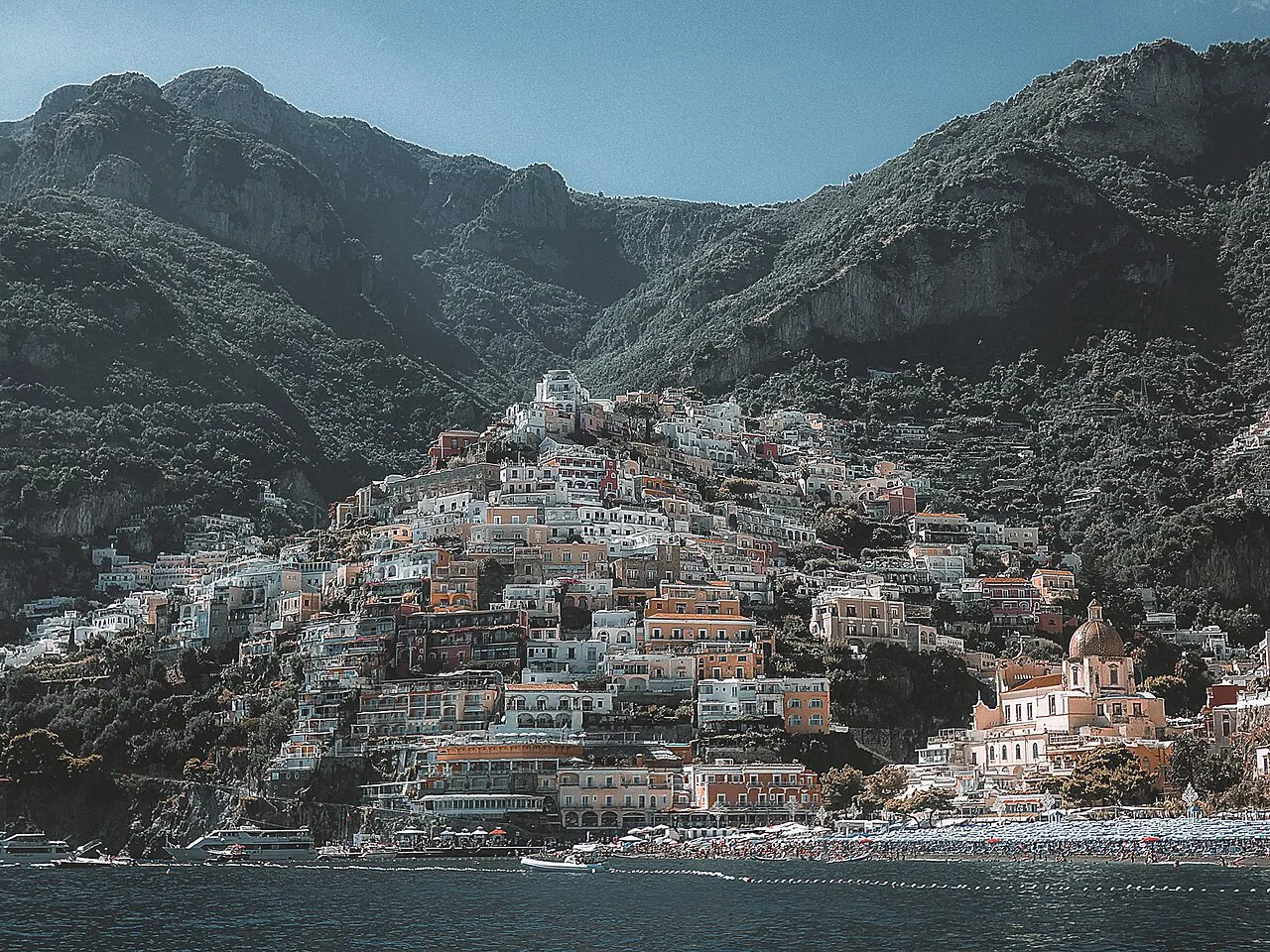 Positano's pastel houses rising up the slope beneath steep Amalfi Coast mountains, seen from the sea