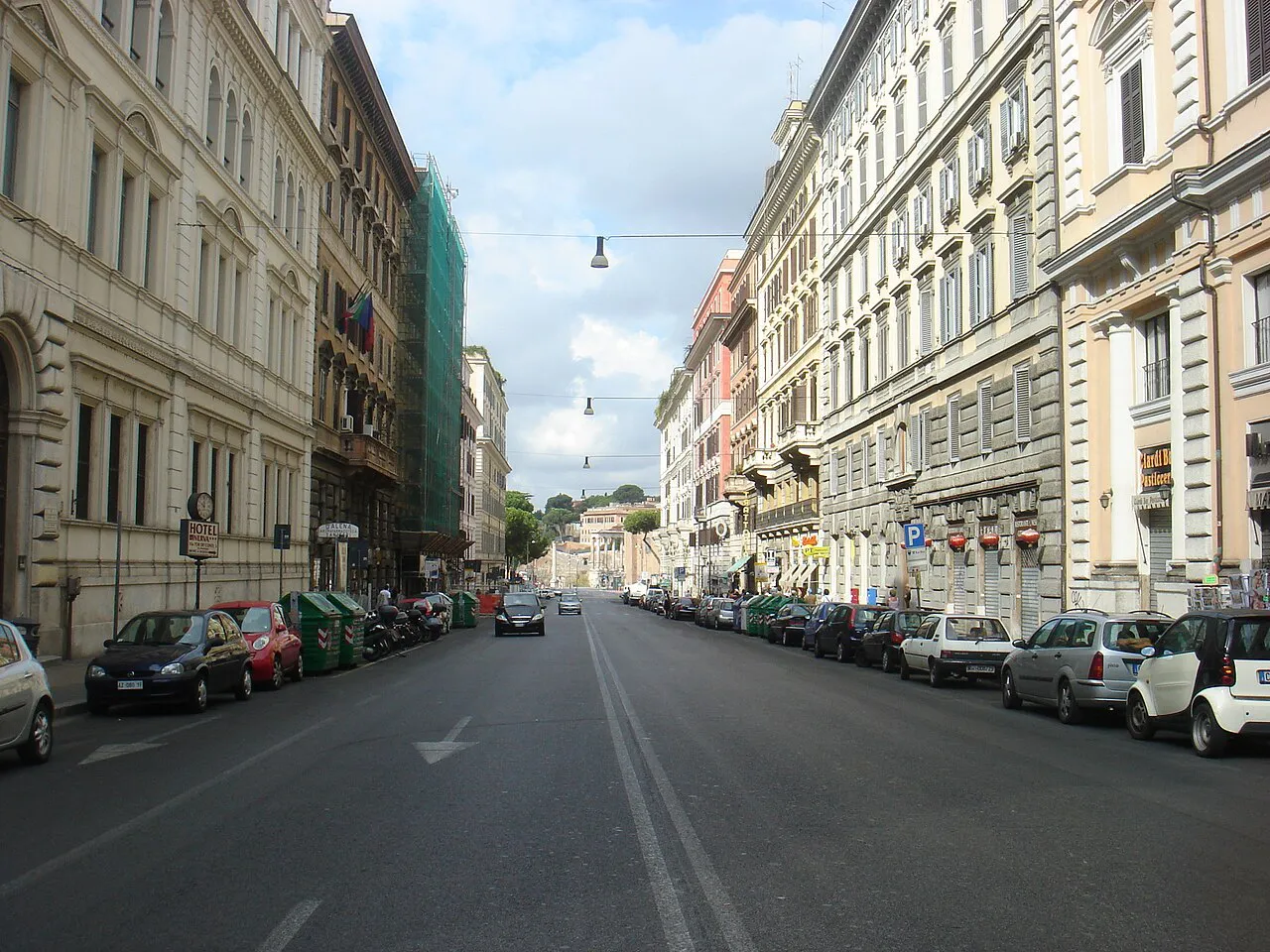 Via Cavour in Rome lined with tall stone apartment buildings and parked cars, sloping towards the Forum