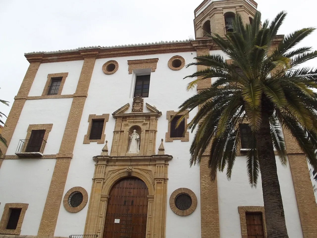 Whitewashed Baroque facade of the Church of La Merced on Plaza de la Merced in Ronda, beside a palm