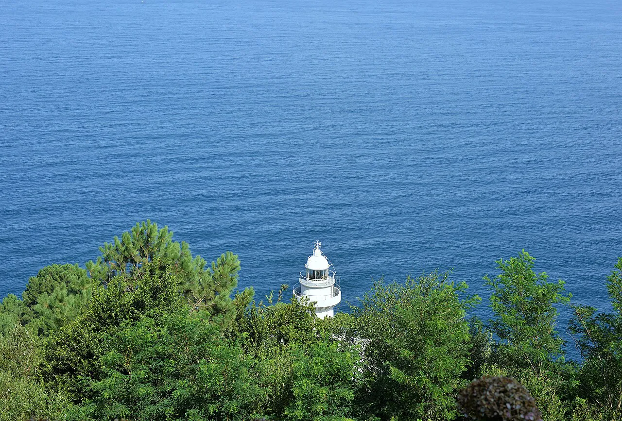 White lighthouse among pine trees above the open sea on Monte Igueldo, San Sebastián