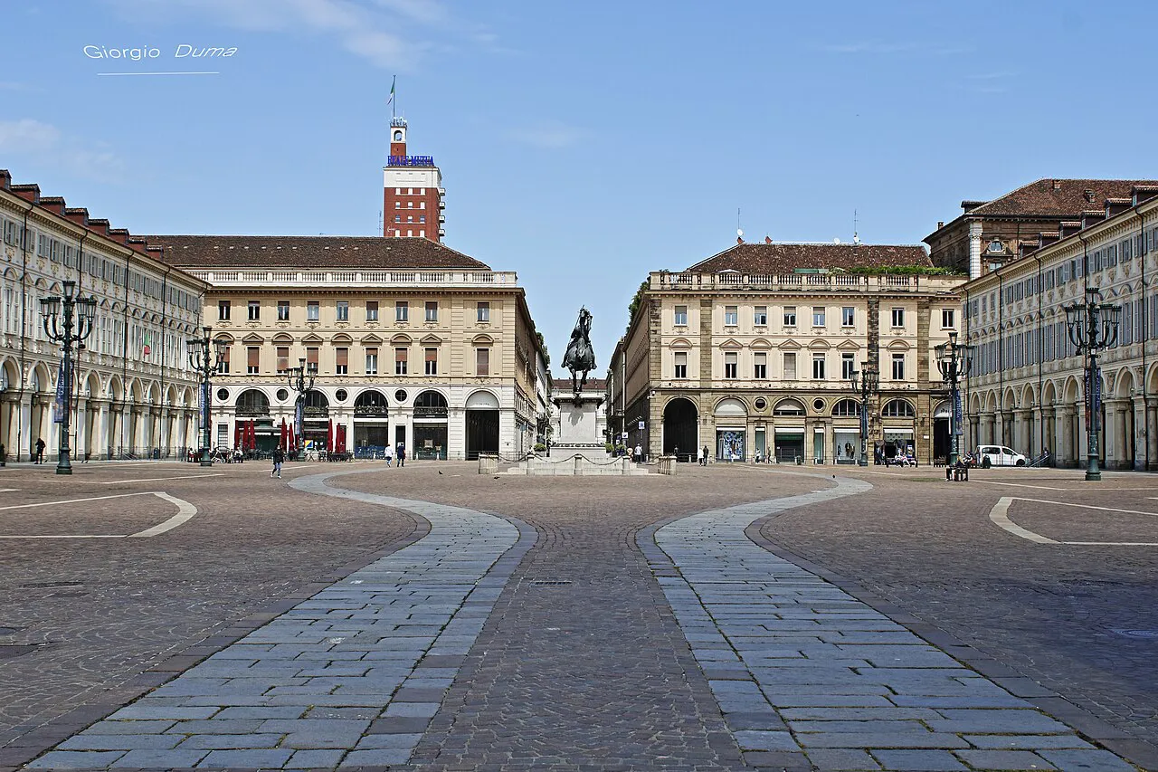 Wide paved expanse of Piazza San Carlo in Turin framed by matching arcaded palazzi under a blue sky