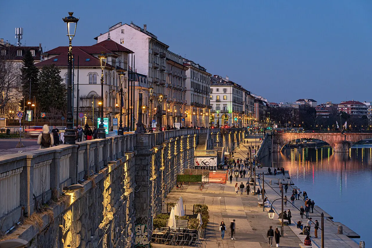 Lamplit riverside embankment of the Murazzi del Po in Turin at dusk, with arcaded buildings above