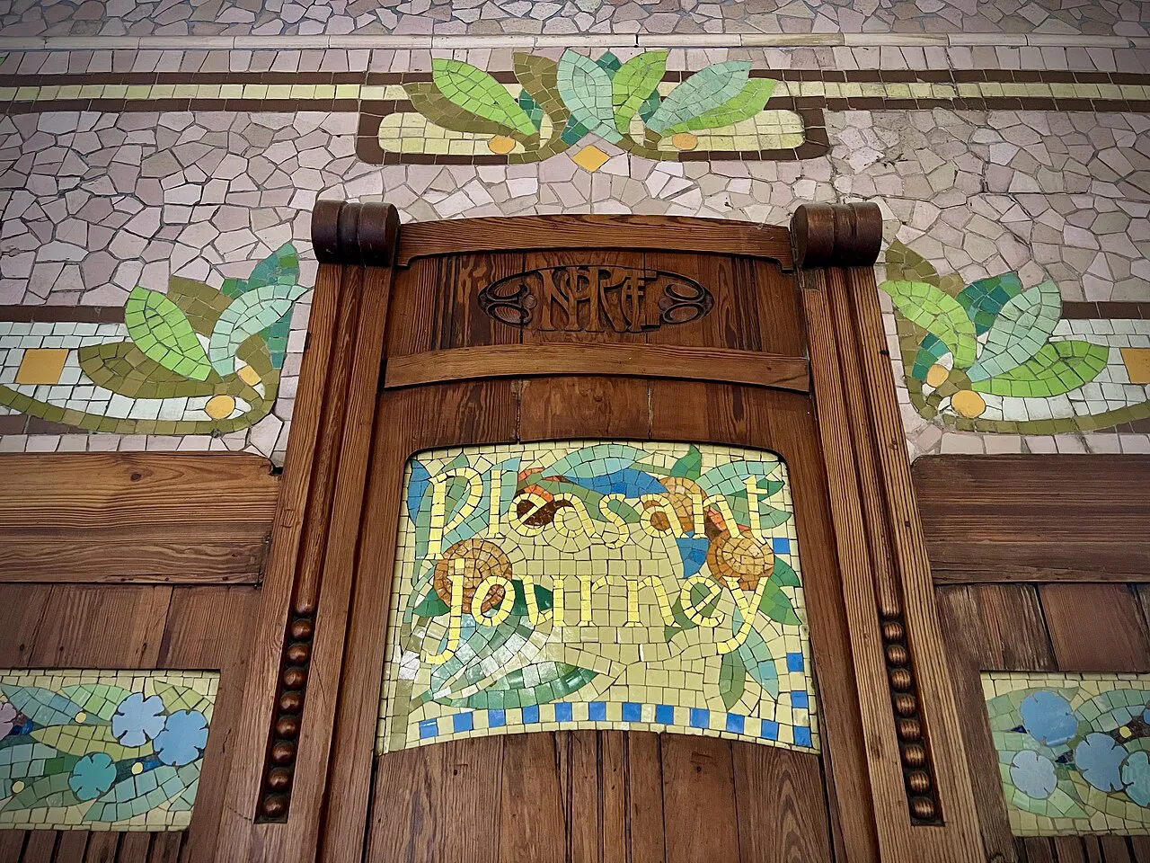 Modernist trencadís mosaic reading Pleasant Journey above a wooden door inside València Nord station