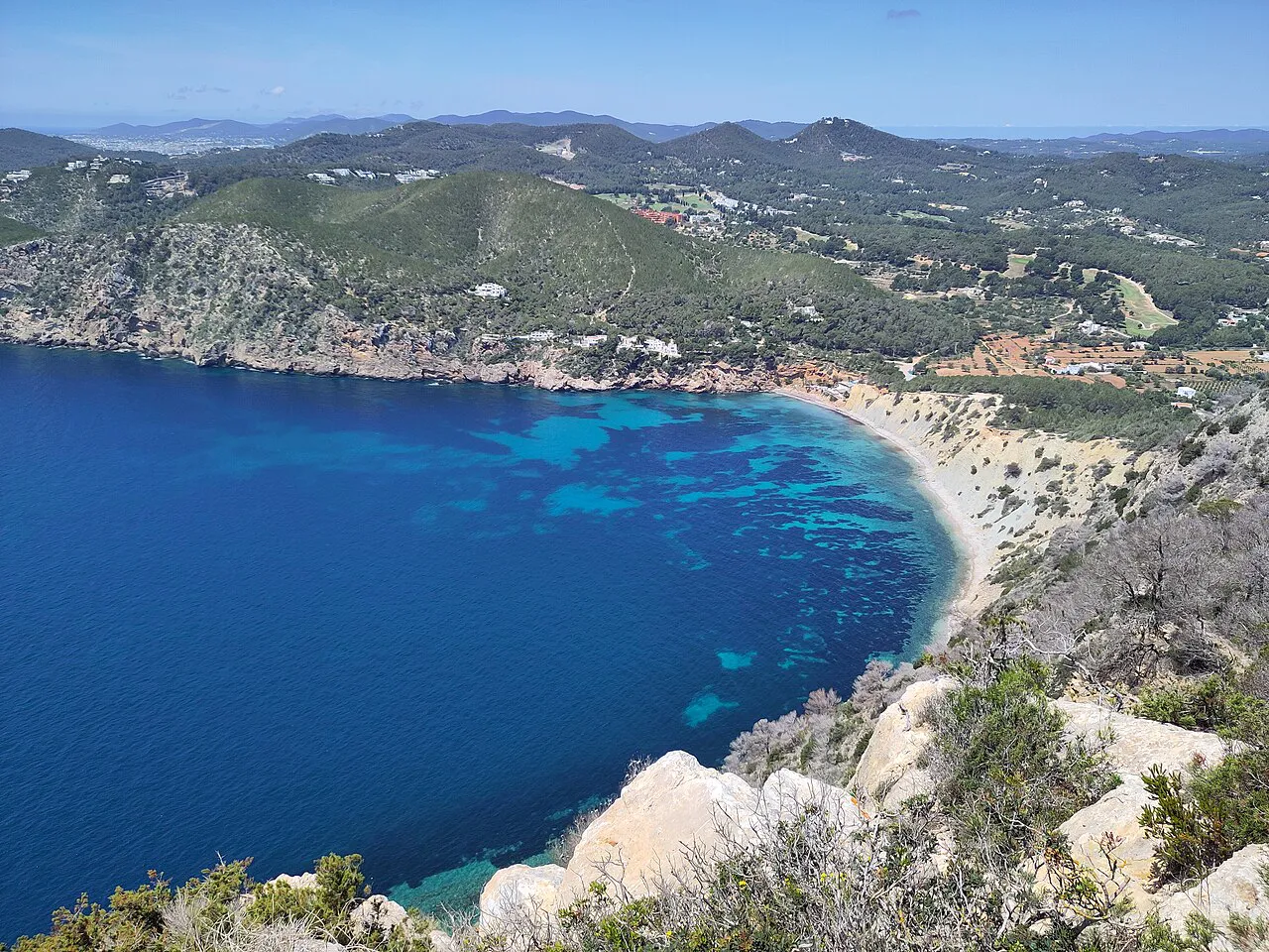 Wide bay of Salt d'en Serra with deep blue water and wooded hills, seen from Cap del Llibrell, Santa Eulària des Riu