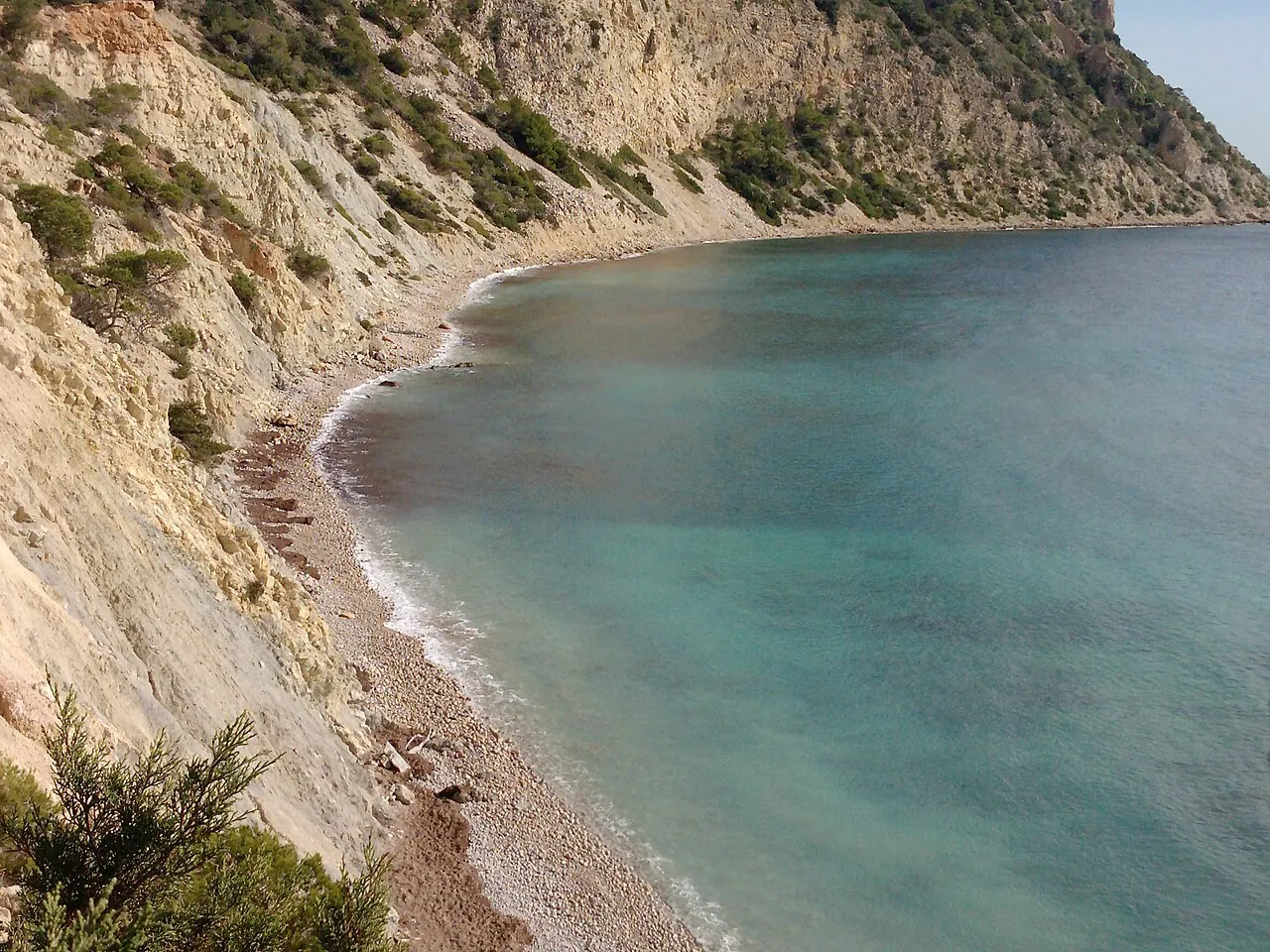 Pebble cove at Sol d'en Serra beneath pale cliffs and pines in Santa Eulària des Riu, Ibiza
