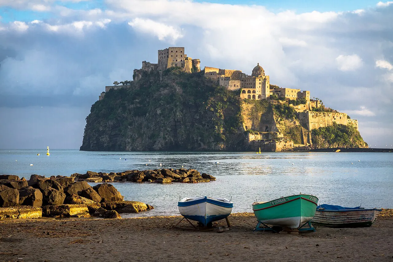 Castello Aragonese on its rocky islet seen from the sand of Spiaggia dei Pescatori, Ischia, with small boats