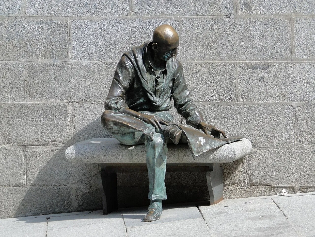 Bronze statue of a seated man reading on a stone bench in Plaza de la Paja, La Latina, Madrid