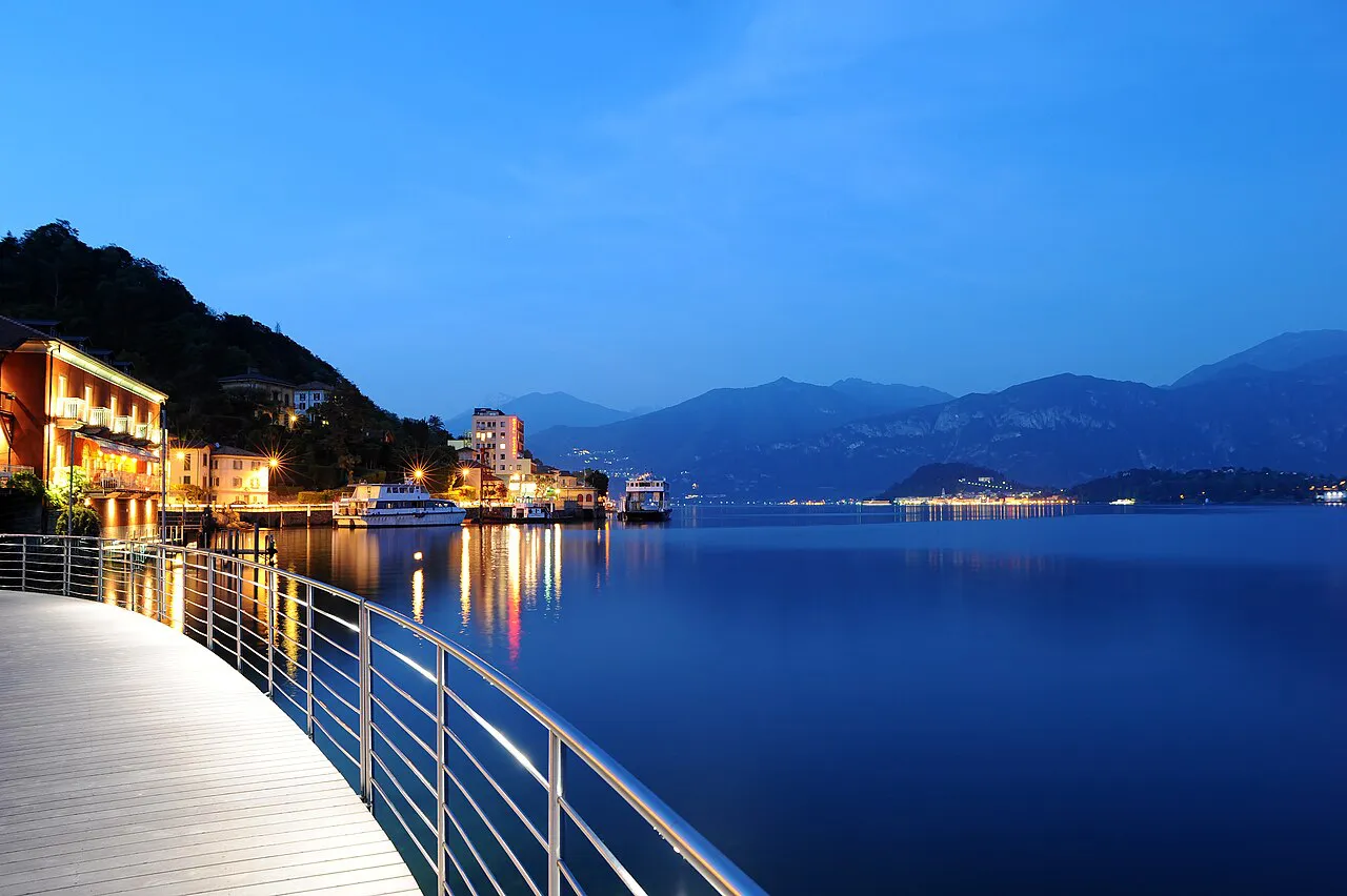 Lakeside walkway in Tremezzo at dusk, with lights reflected in Lake Como and mountains beyond
