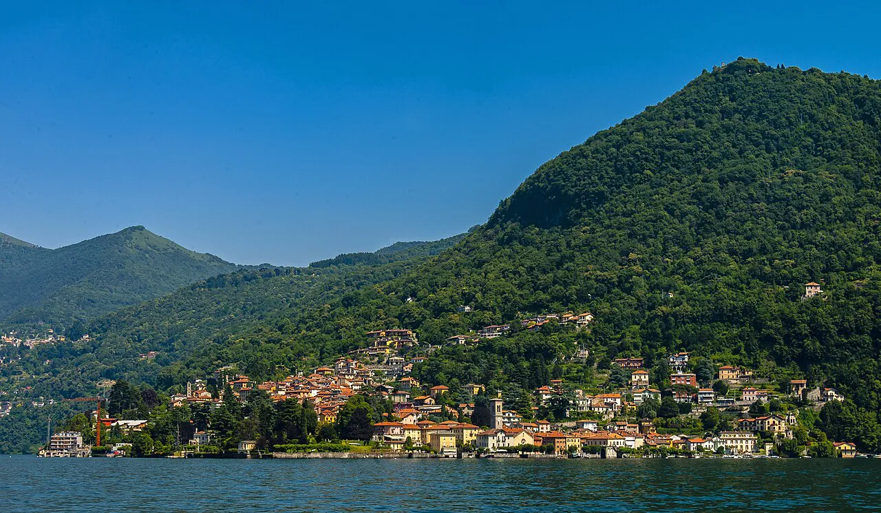 The village of Torno clustered on the shore of Lake Como below a forested hill