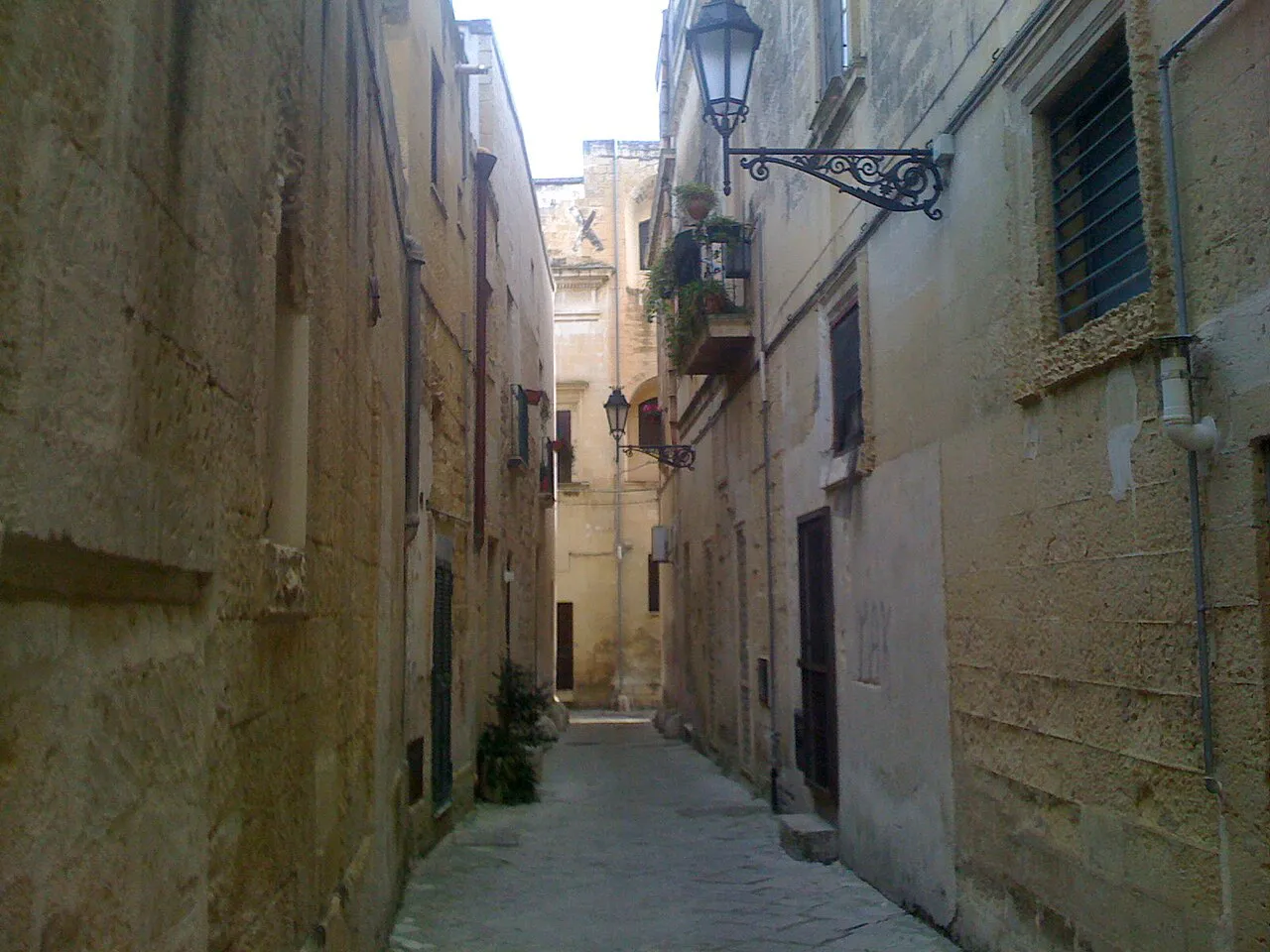 Narrow lane of pale limestone buildings with a wrought-iron lamp in Lecce's historic centre