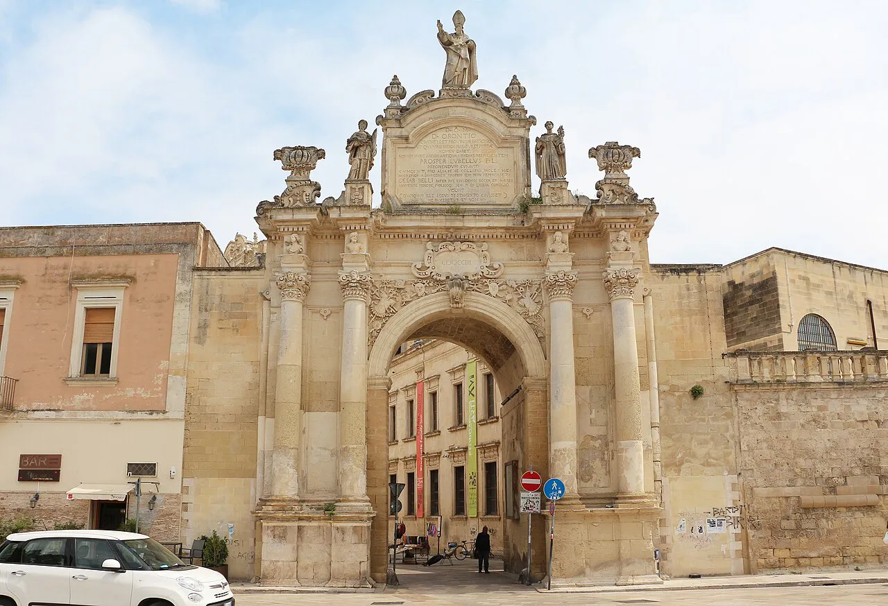 Baroque Porta Rudiae city gate in Lecce crowned with statues, with old town buildings beside it
