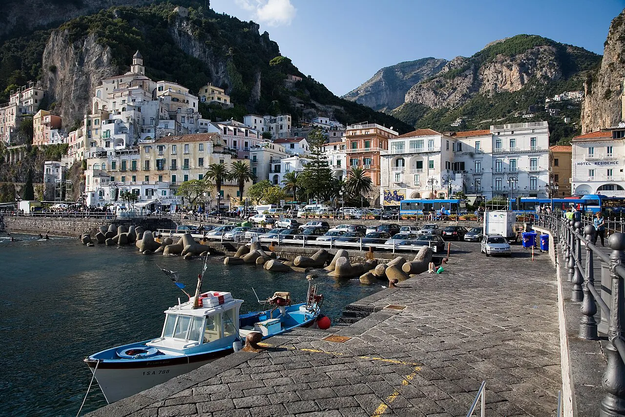 Amalfi's white town and cliffs seen from the harbour pier, with small boats moored alongside