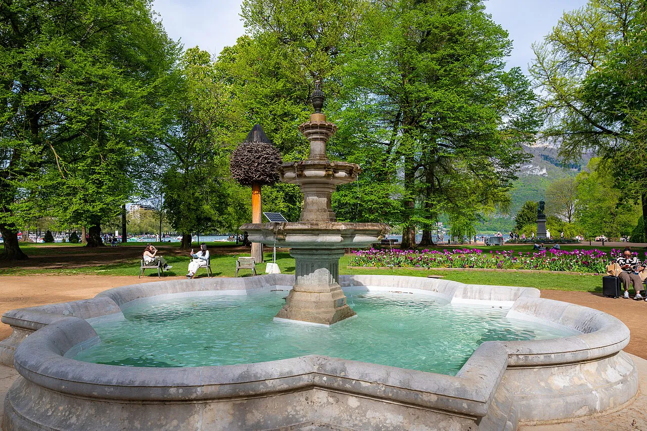 Stone fountain among flowerbeds and tall trees in the Jardins de l'Europe, Annecy