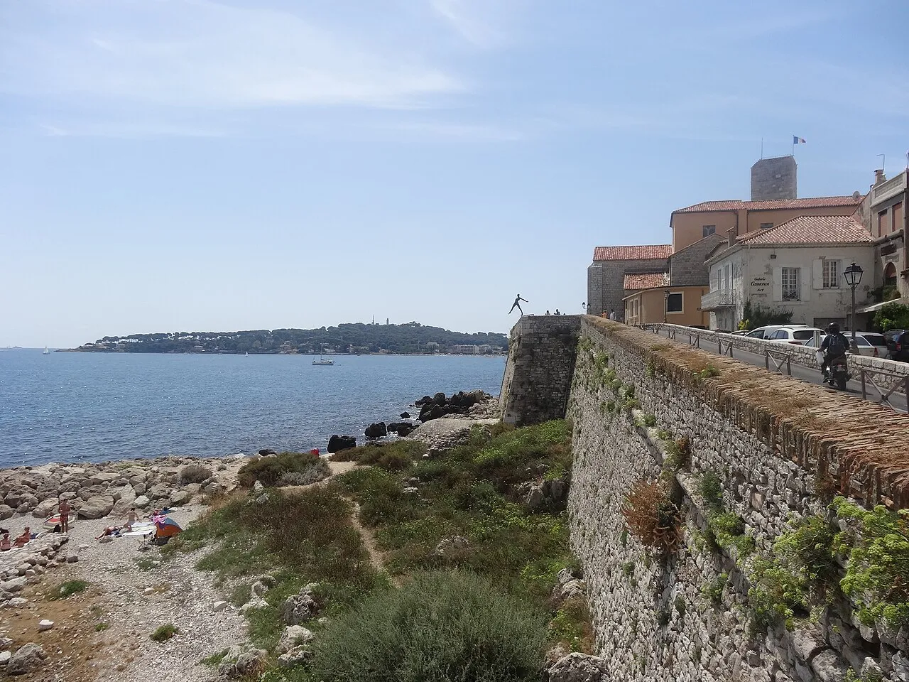 Old stone ramparts of Antibes above a rocky shore, with Cap d'Antibes on the horizon