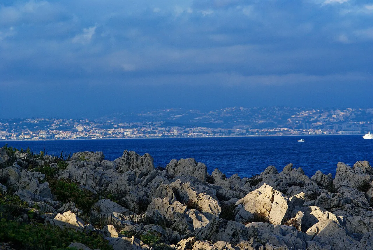 Jagged white limestone rocks on the Cap d'Antibes shore with the Baie des Anges and Nice beyond
