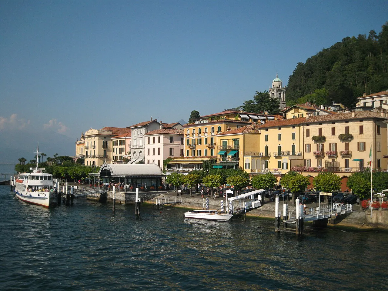 Bellagio's ferry landing and pastel lakefront buildings beneath a wooded hill on Lake Como