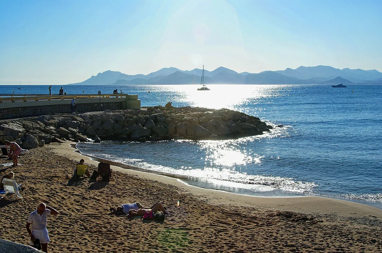 Sandy beach and breakwater on the Croisette in Cannes, with sunlit sea and the Esterel hills beyond