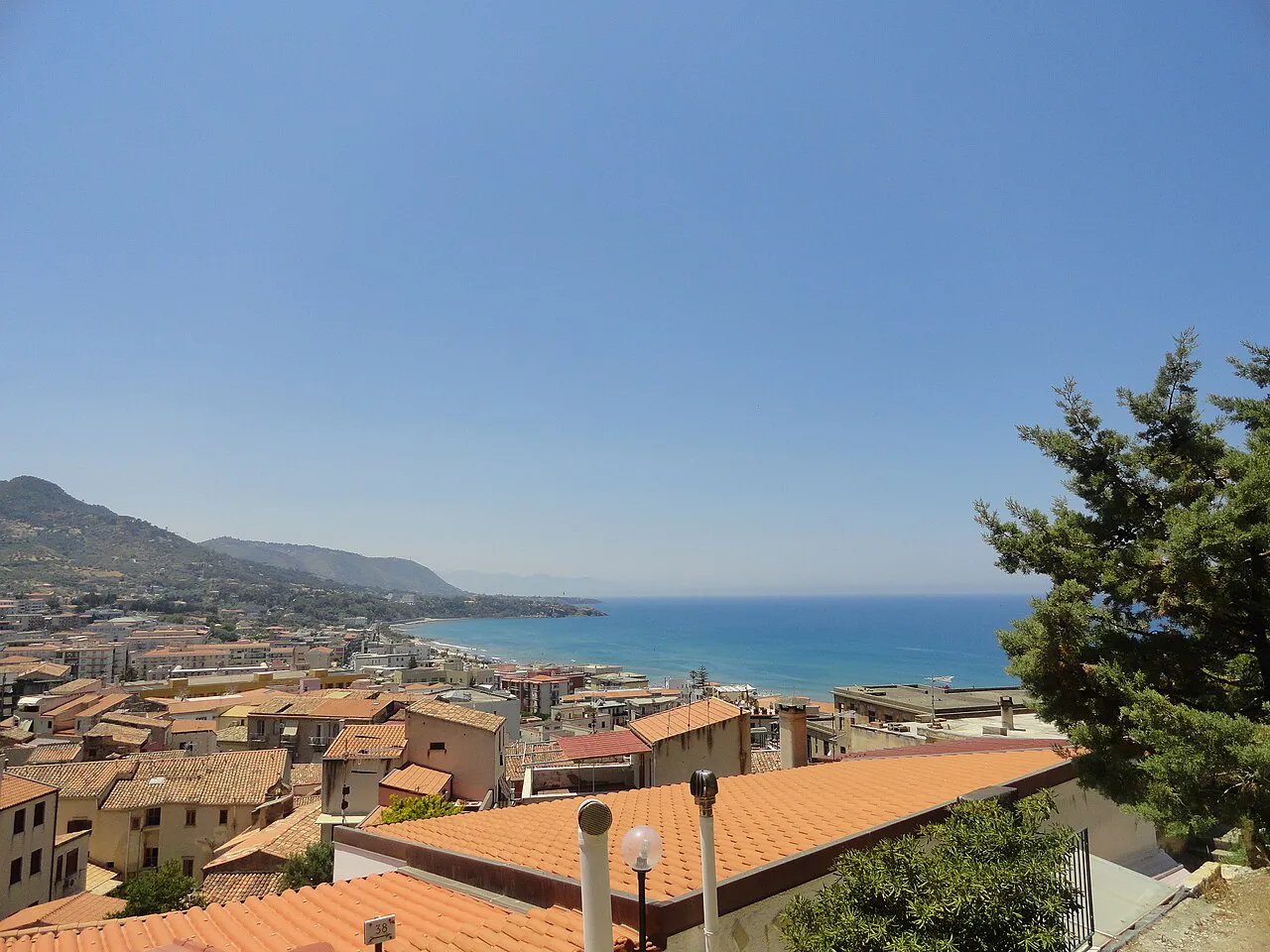 Terracotta rooftops of Cefalù seen from above, with the coastline and sea stretching east