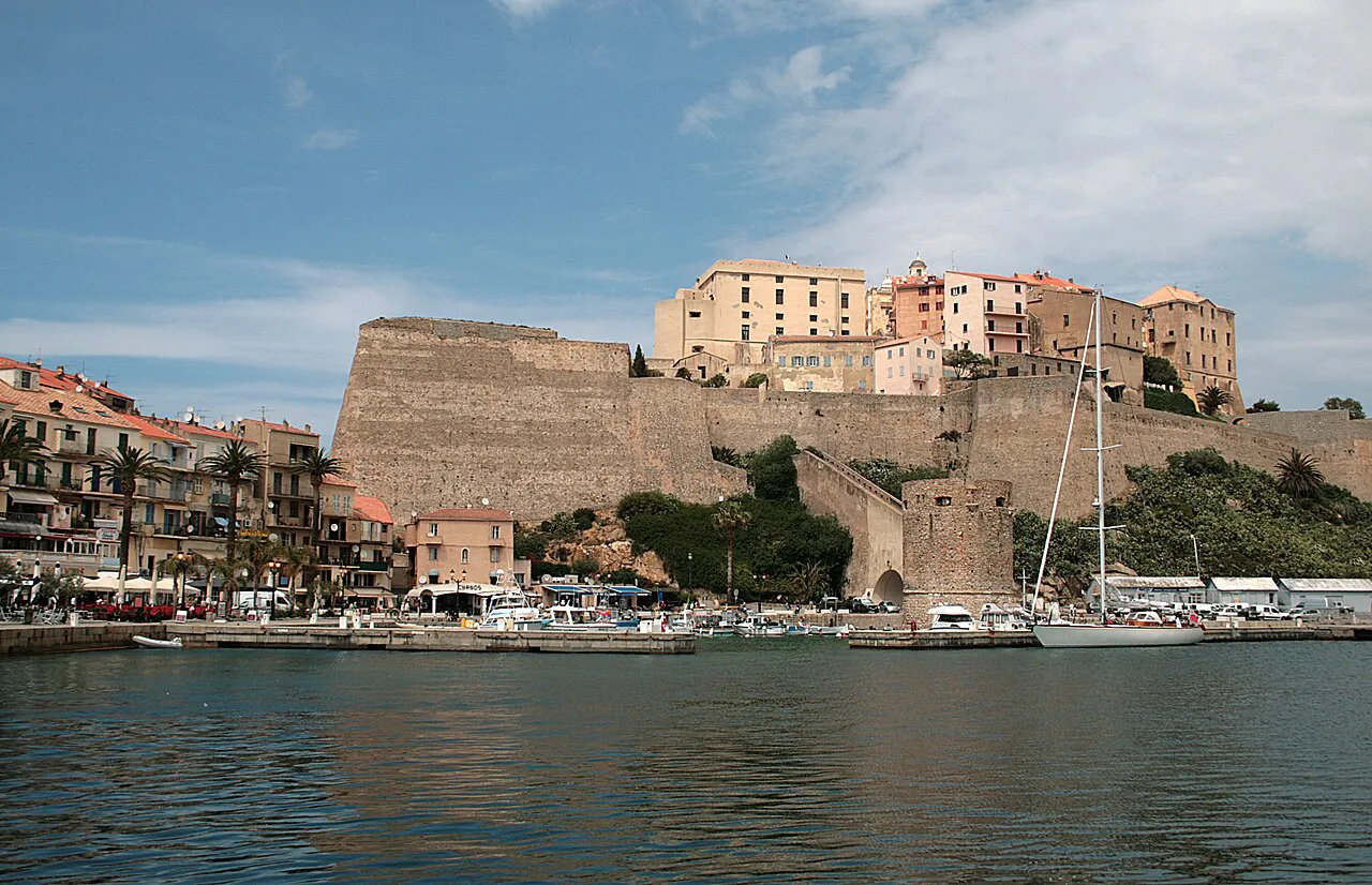 Massive walls of Calvi citadel rising behind the harbour and waterfront houses