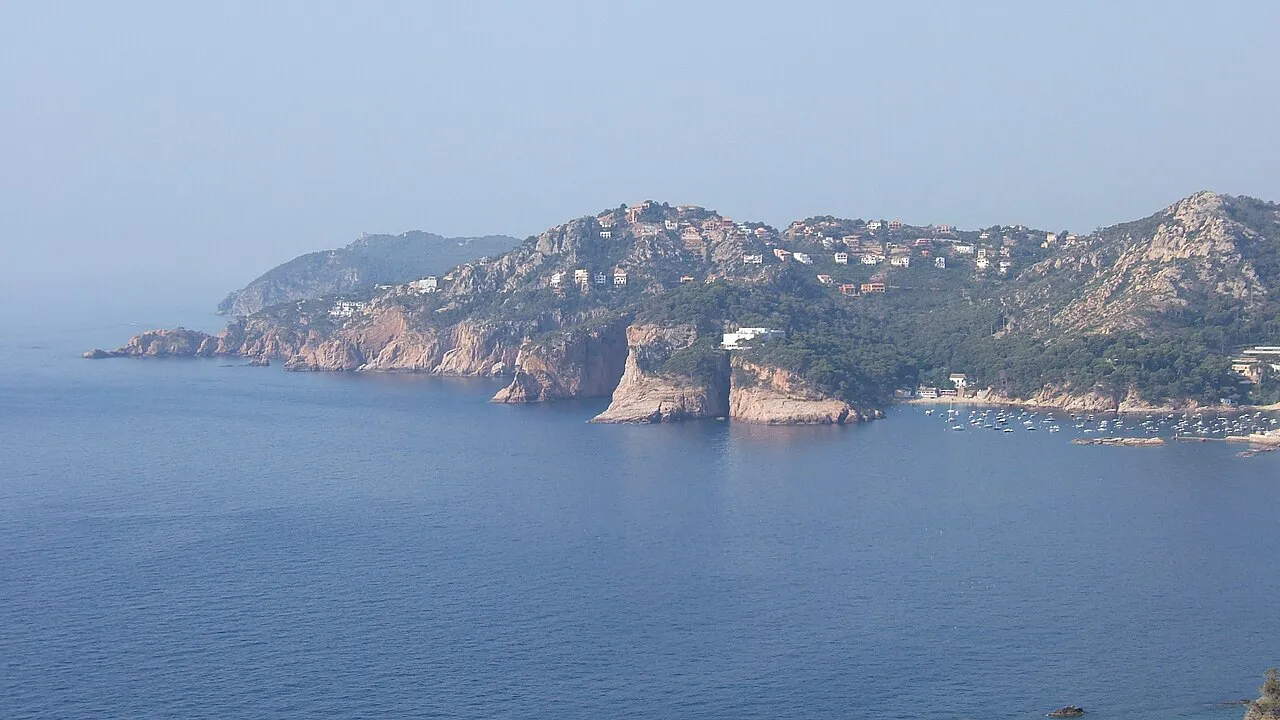 Rocky headland of Punta des Mut rising from calm blue sea at Aiguablava, Begur