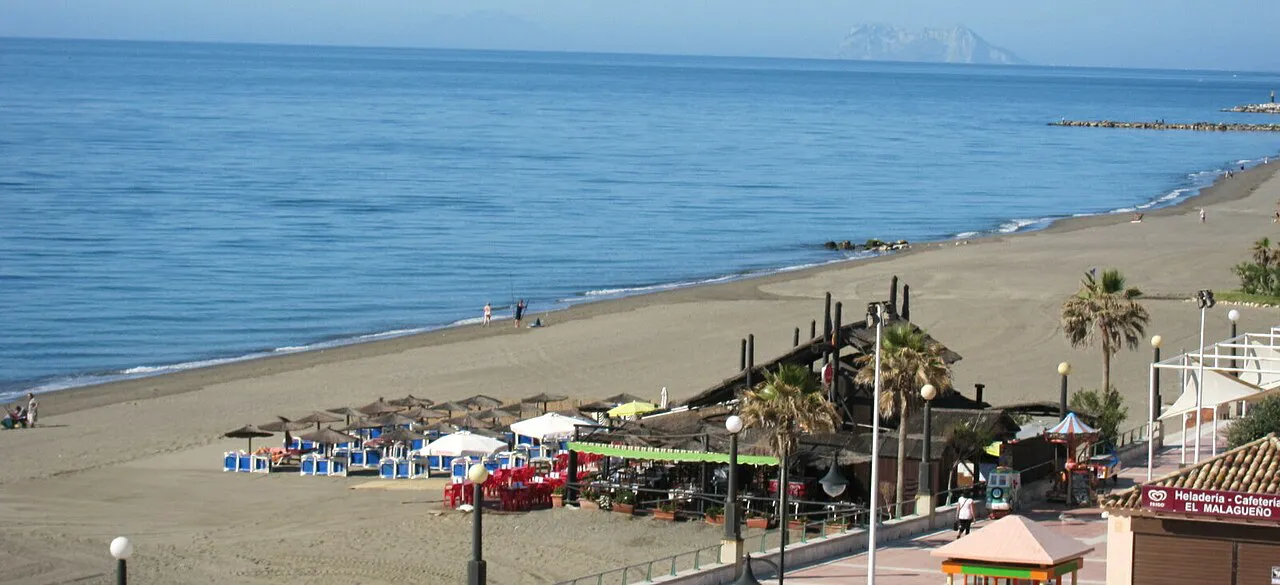 Long sandy beach in Estepona with beach bars and calm blue sea, Gibraltar faint on the horizon